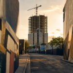 Calle de Wynwood en Miami al atardecer, con muros pintados desenfocados en primer plano y una torre residencial en construcción al fondo.